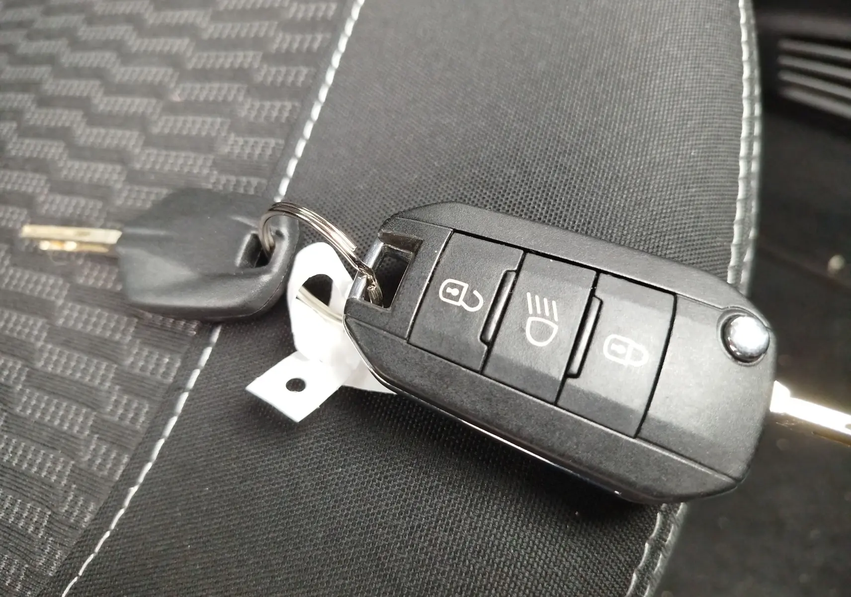 Clé de contact Peugeot 208 posée sur un siège en tissu noir, vue rapprochée du boîtier télécommande.