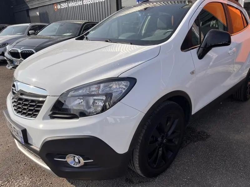 Opel Mokka blanc glacier vue 3/4 avant droit, jantes noires et calandre chromée visible.