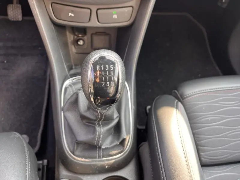 Vue rapprochée du levier de vitesse manuel noir de l’Opel Mokka 2015, avec coutures blanches et accoudoir en cuir gris.