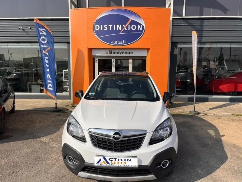 Opel Mokka blanc glacier vu de face, calandre chromée et phares halogènes, devant un bâtiment orange Distinxion.