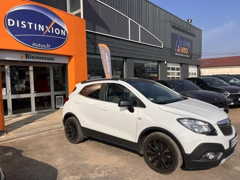 Opel Mokka blanc glacier en vue 3/4 avant droit, avec jantes noires et barres de toit visibles.