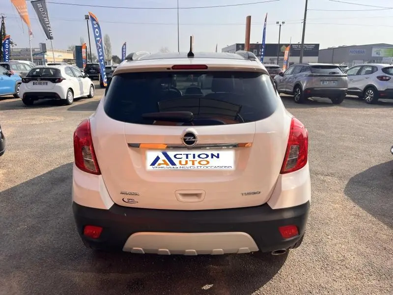 Vue arrière d'un Opel Mokka blanc Glacier avec feux rouges et lunette arrière surteintée, stationné en extérieur.