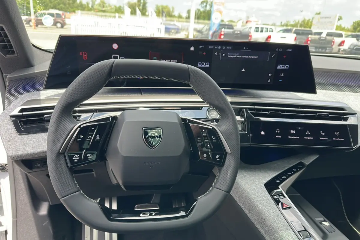 Vue intérieure centrée sur le volant cuir multifonctions du Peugeot 5008 Hybrid 145 GT avec tableau de bord numérique.