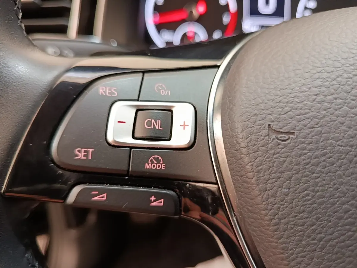 Gros plan sur les commandes du régulateur de vitesse au volant cuir d’une Volkswagen Polo noire, version Carat.