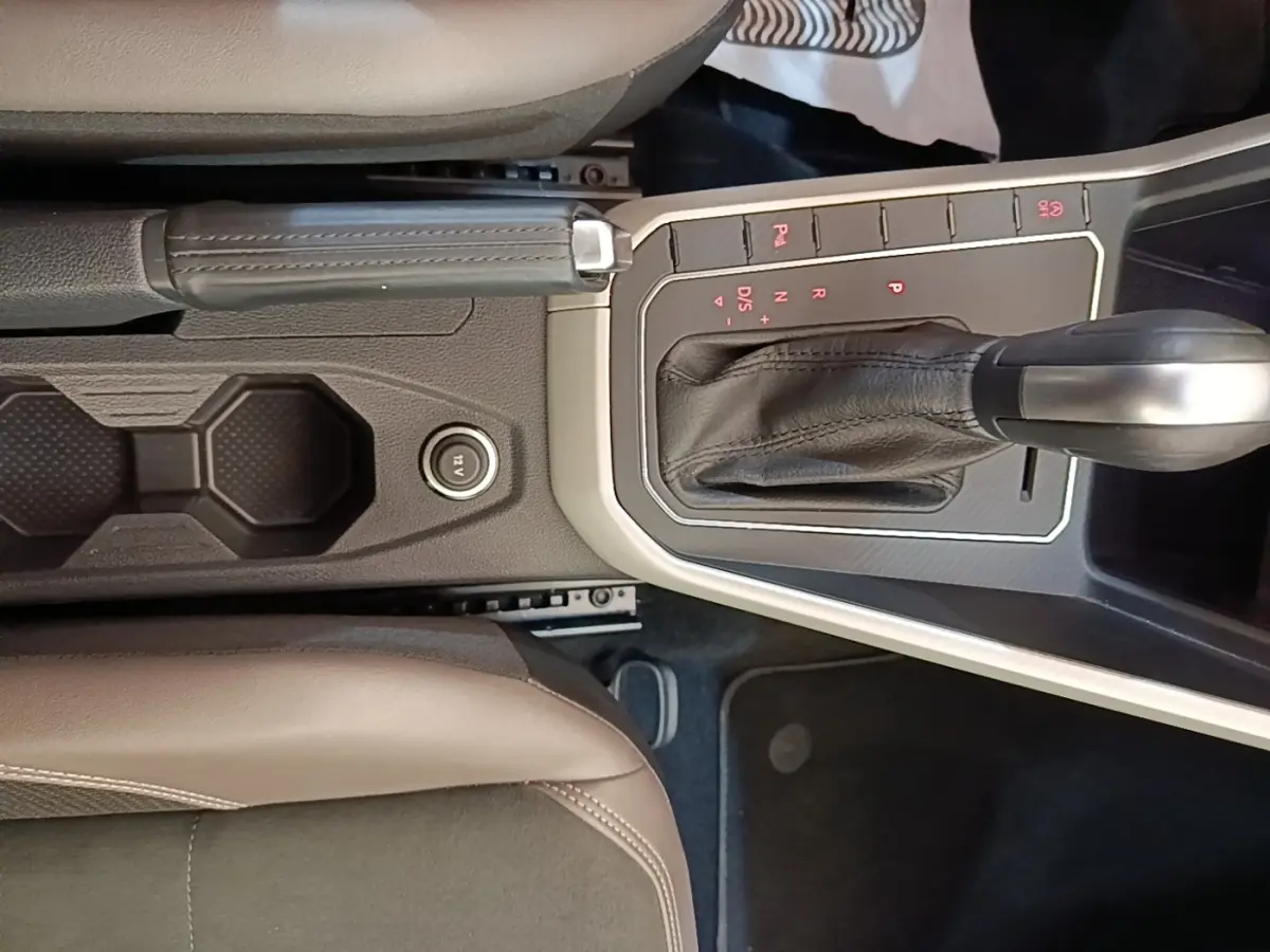 Vue intérieure centrée sur la console centrale de la Volkswagen Polo noire, avec levier de vitesse automatique et frein à main cuir.