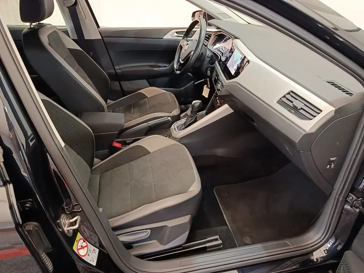 Vue intérieure côté conducteur de la Volkswagen Polo noire 2020, montrant sièges et tableau de bord moderne.