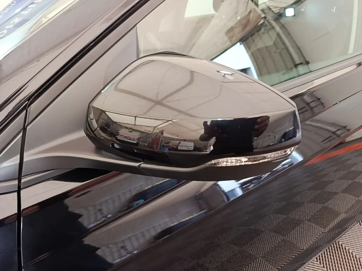 Rétroviseur côté gauche noir brillant de Volkswagen Polo 1.0 TSI 115 DSG7 Carat, reflet intérieur d'atelier visible.