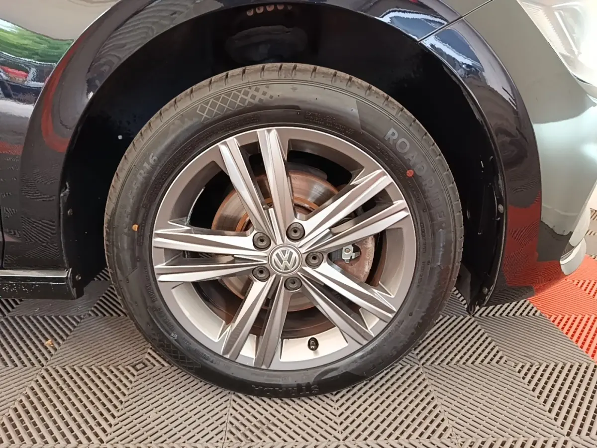 Gros plan sur la roue avant droite d’une Volkswagen Polo noire, mettant en valeur la jante alliage à cinq doubles branches.