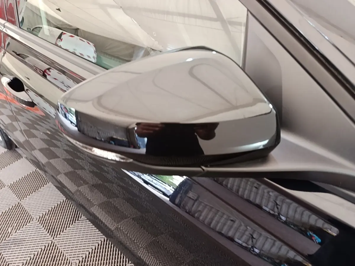 Gros plan sur le rétroviseur droit noir brillant d'une Volkswagen Polo 2020, reflet d'un garage intérieur.