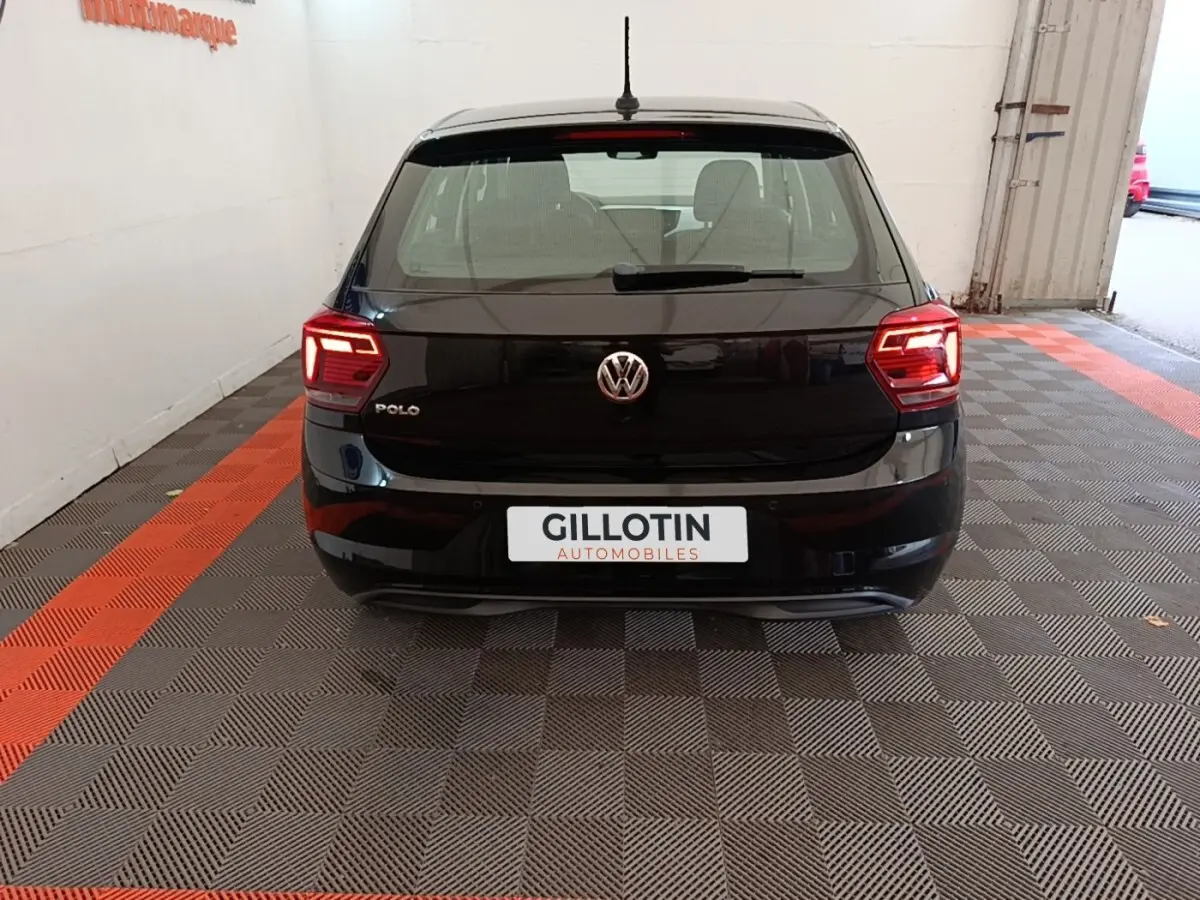 Vue arrière d'une Volkswagen Polo noire 2020 avec feux LED allumés, stationnée sur sol à damier gris et rouge.