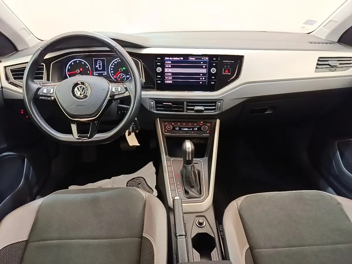 Vue intérieure avant de la Volkswagen Polo noire, tableau de bord moderne avec écran tactile central et volant multifonctions.