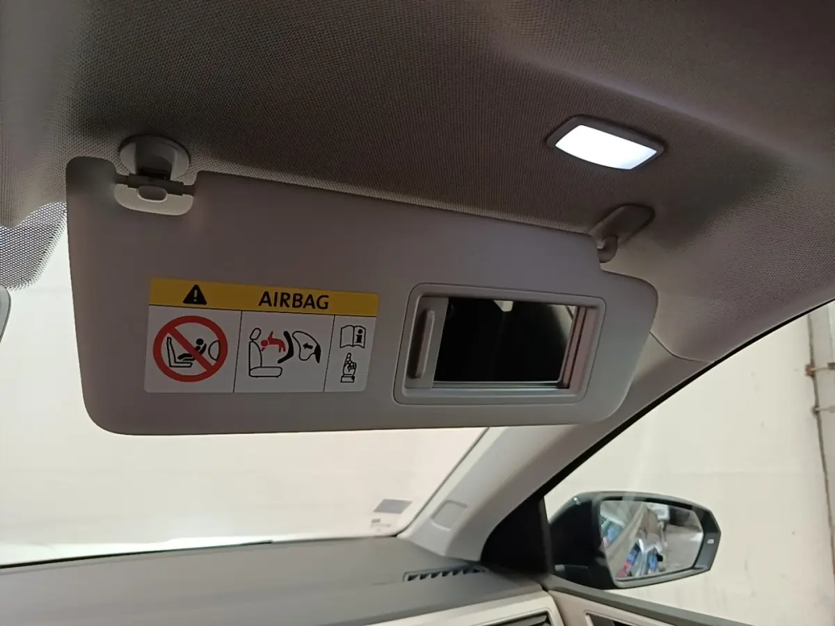 Vue intérieure côté passager du pare-soleil beige avec miroir et éclairage, rétroviseur extérieur noir visible.