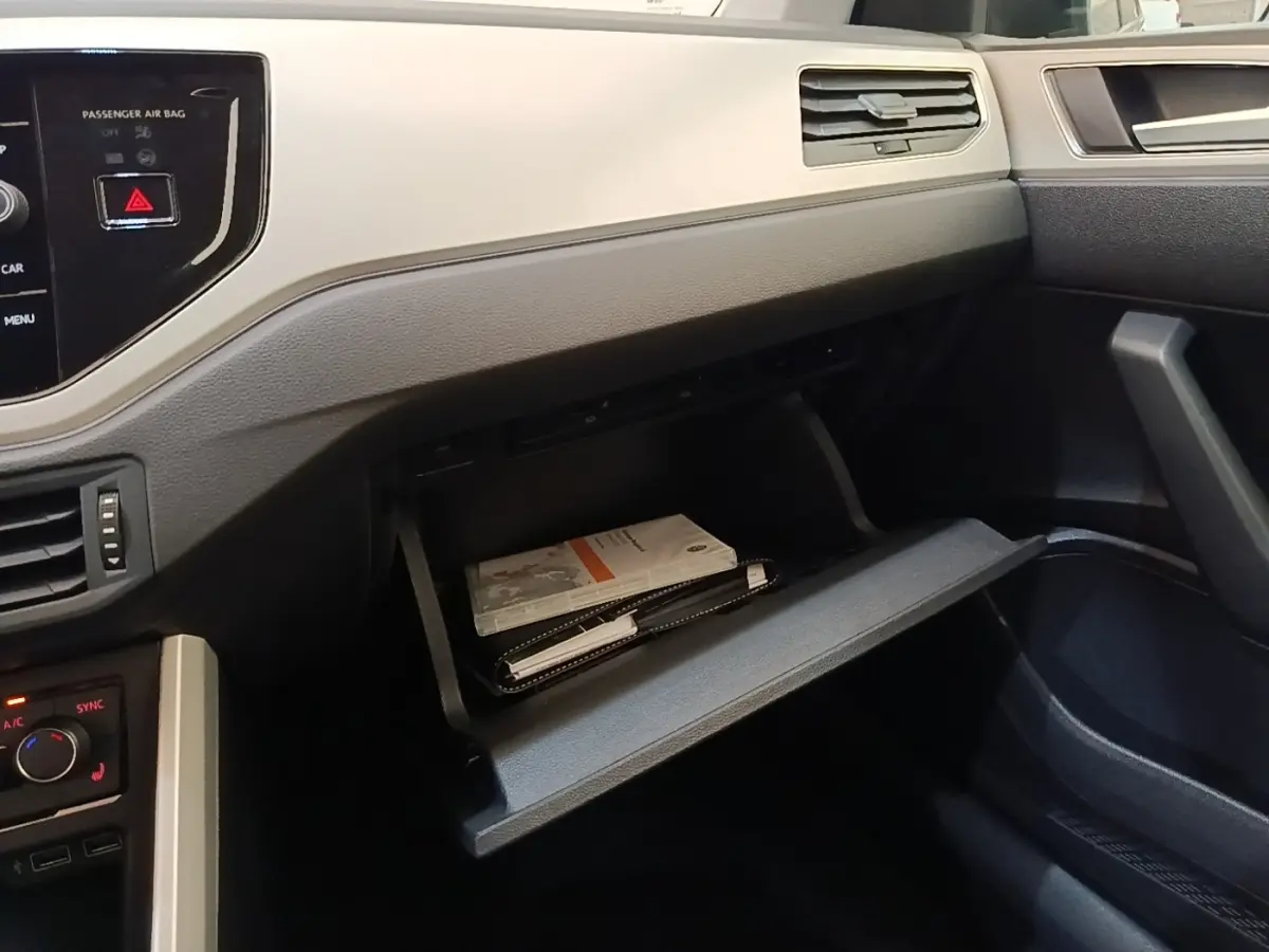 Vue intérieure côté passager de la Volkswagen Polo noire 2020, boîte à gants ouverte avec documents visibles.