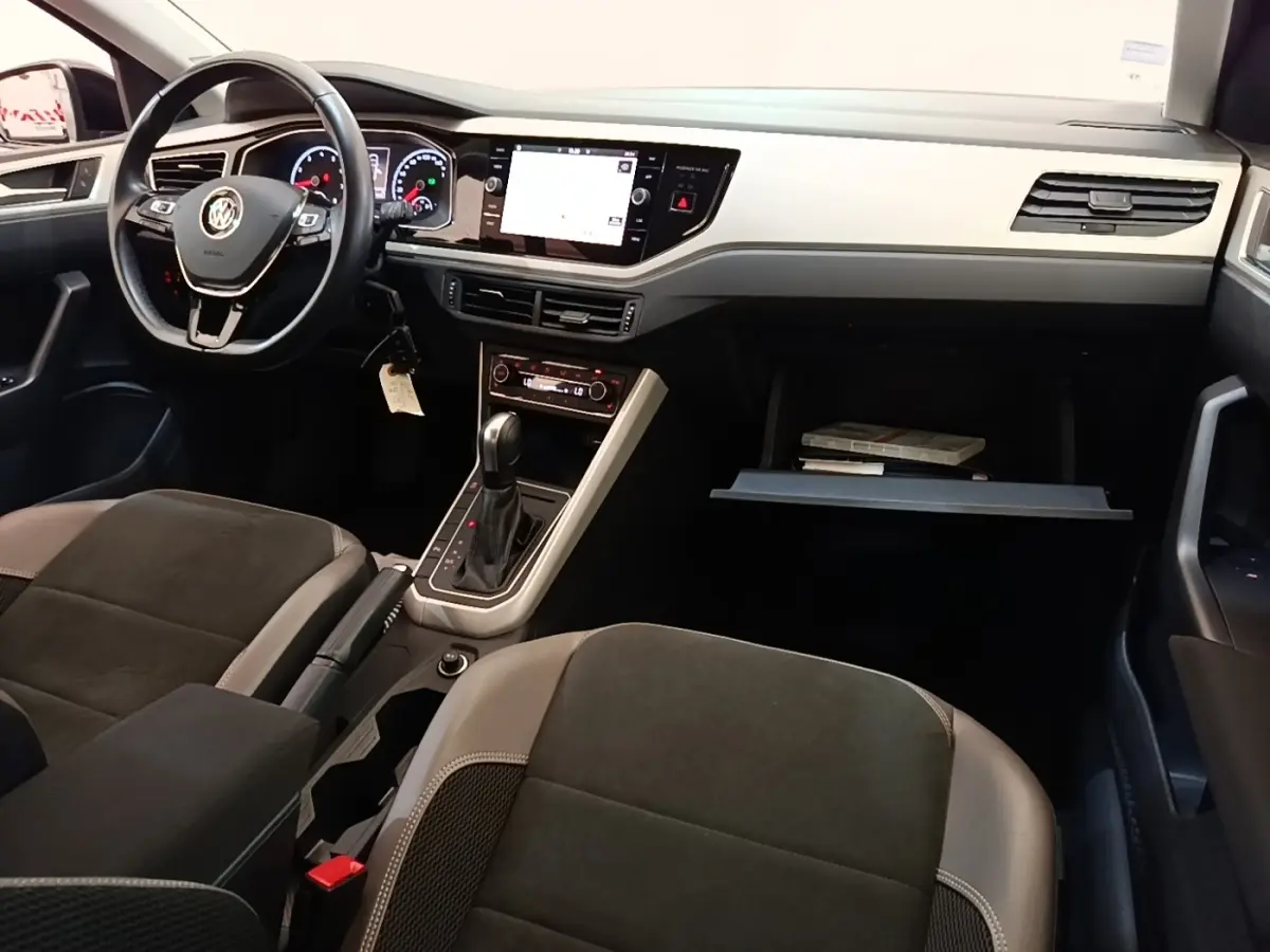 Vue intérieure avant droite de la Volkswagen Polo noire 2020, tableau de bord clair avec écran tactile et volant multifonctions.