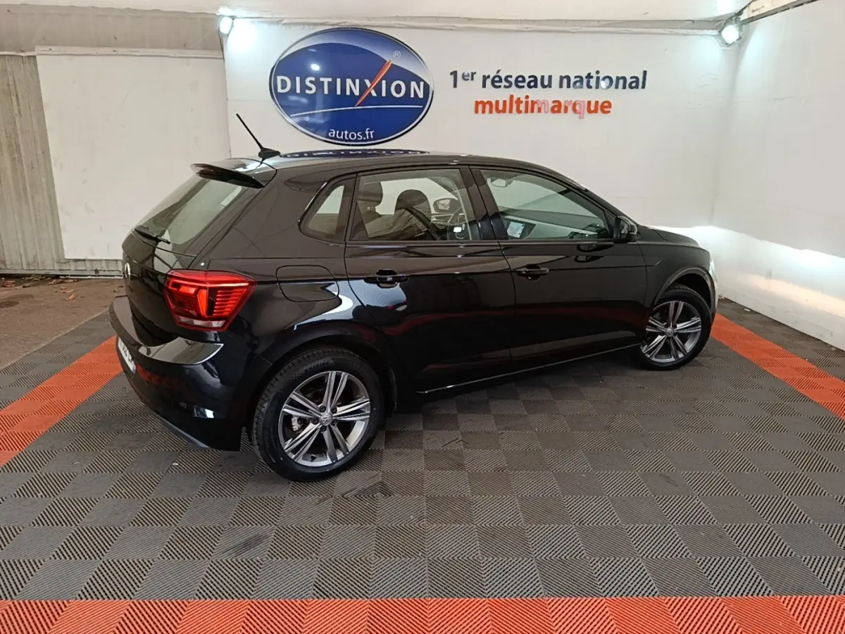 Volkswagen Polo noir vue 3/4 arrière droit en intérieur avec jantes alliage et feux arrière LED allumés.