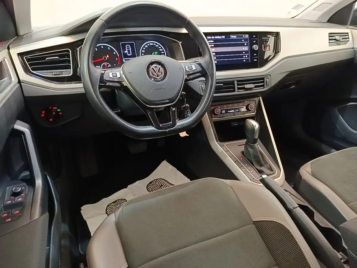 Vue intérieure avant de la Volkswagen Polo noire 2020, tableau de bord avec écran tactile et volant multifonctions en cuir.