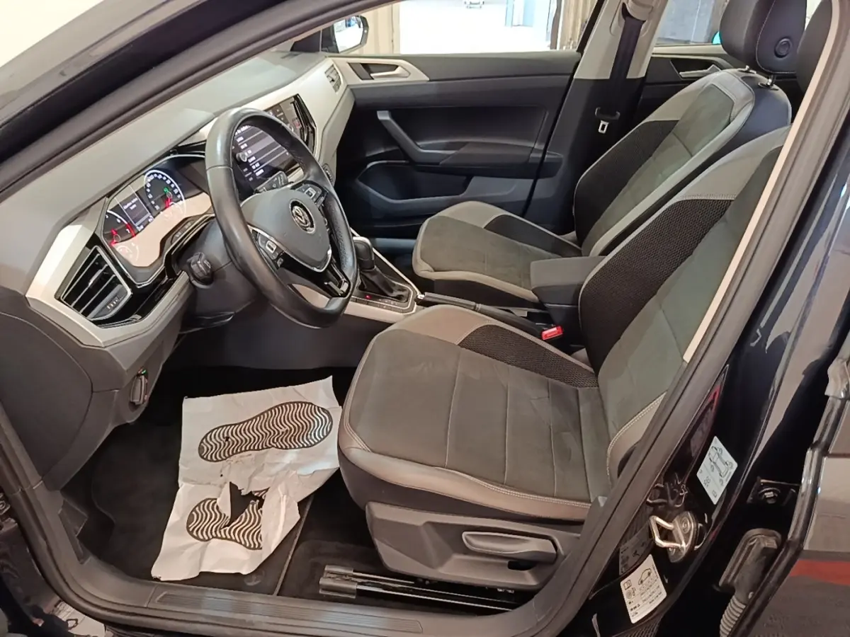 Vue intérieure côté conducteur d'une Volkswagen Polo noire 2020, montrant sièges tissu et tableau de bord moderne.