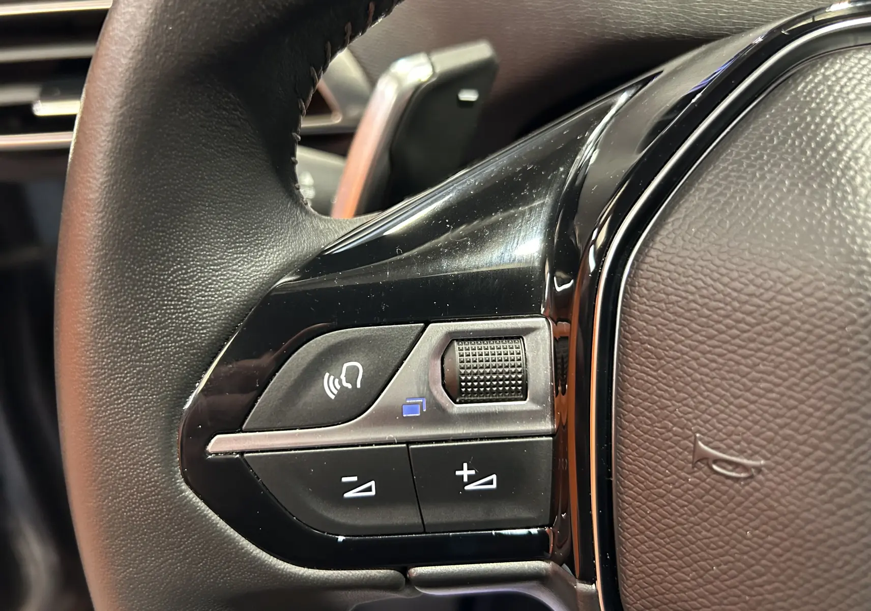 Détail du volant noir du Peugeot 3008 Hybrid 2024 montrant les commandes audio et téléphone côté gauche.