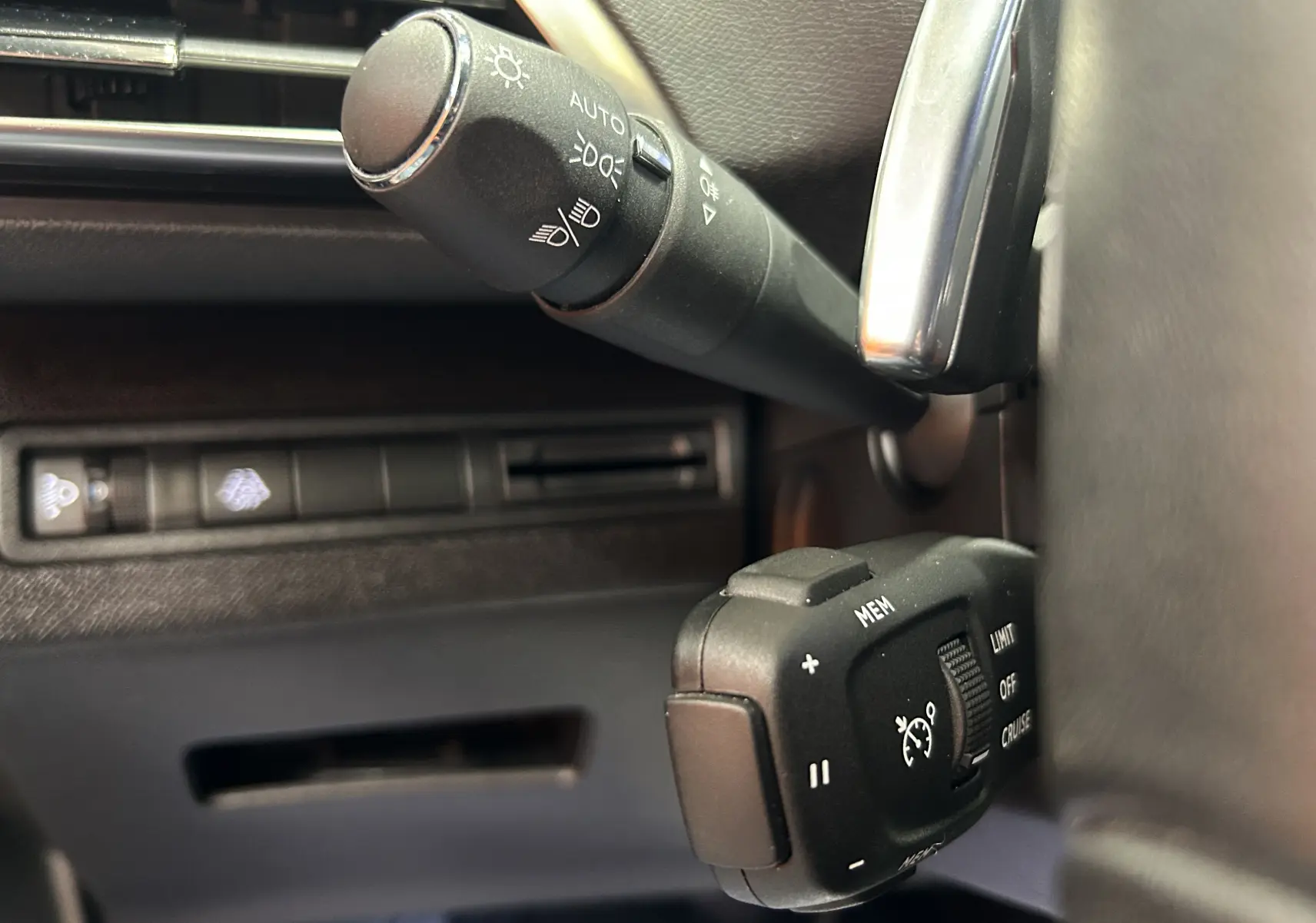 Gros plan sur les commandes de régulateur de vitesse et éclairage du Peugeot 3008 Hybrid gris, côté gauche du volant.