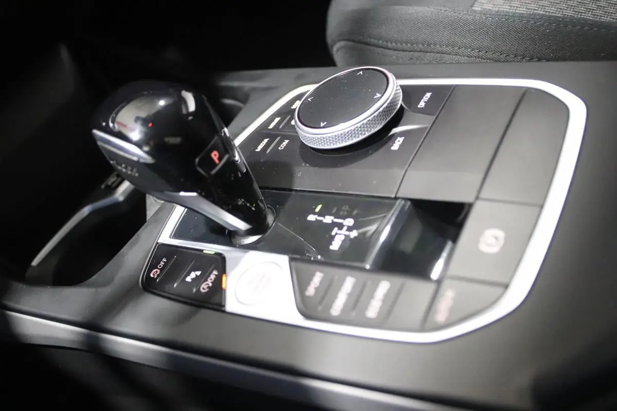 Gros plan sur la console centrale noire de la BMW Série 1 116d 2023 avec levier de vitesse automatique et molette de contrôle.
