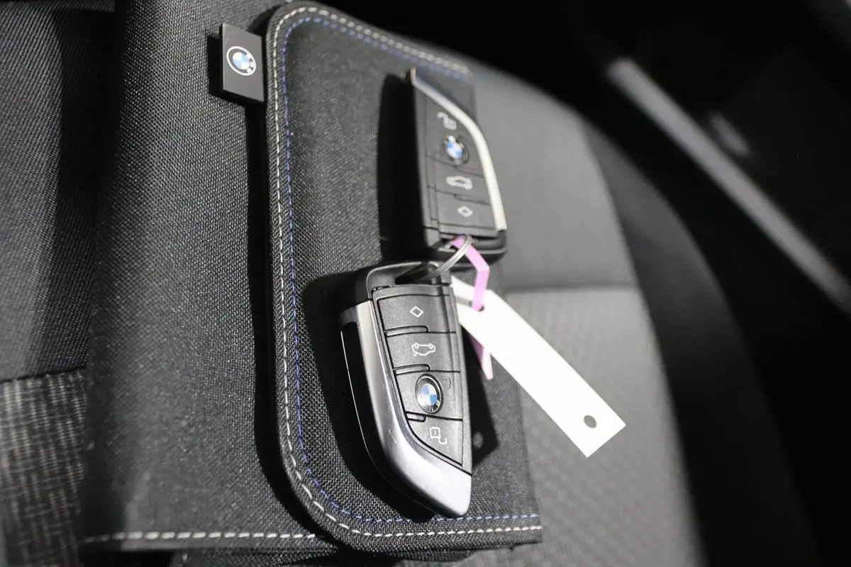 Gros plan sur deux clés BMW posées sur un porte-clés en tissu noir avec surpiqûres bleues, intérieur de siège gris.