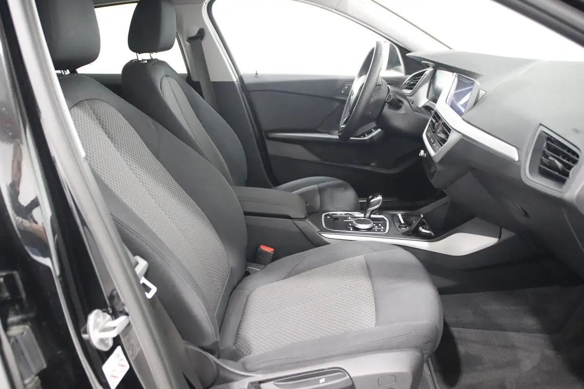 Vue intérieure côté gauche de la BMW Série 1 noire 116d 2023, montrant sièges tissu et console centrale avec boîte auto.
