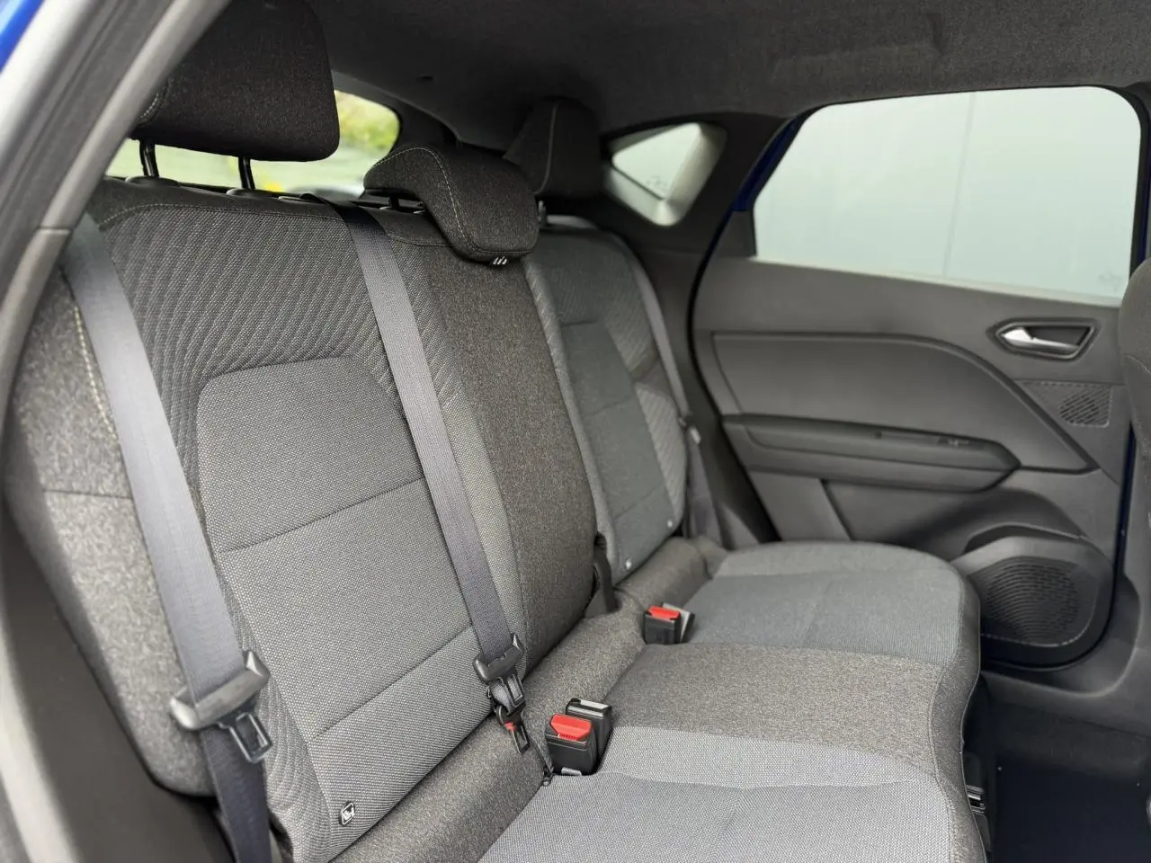 Vue intérieure côté droit des sièges arrière gris du Renault Captur Bleu Iron 2026 avec ceintures et porte arrière visible.