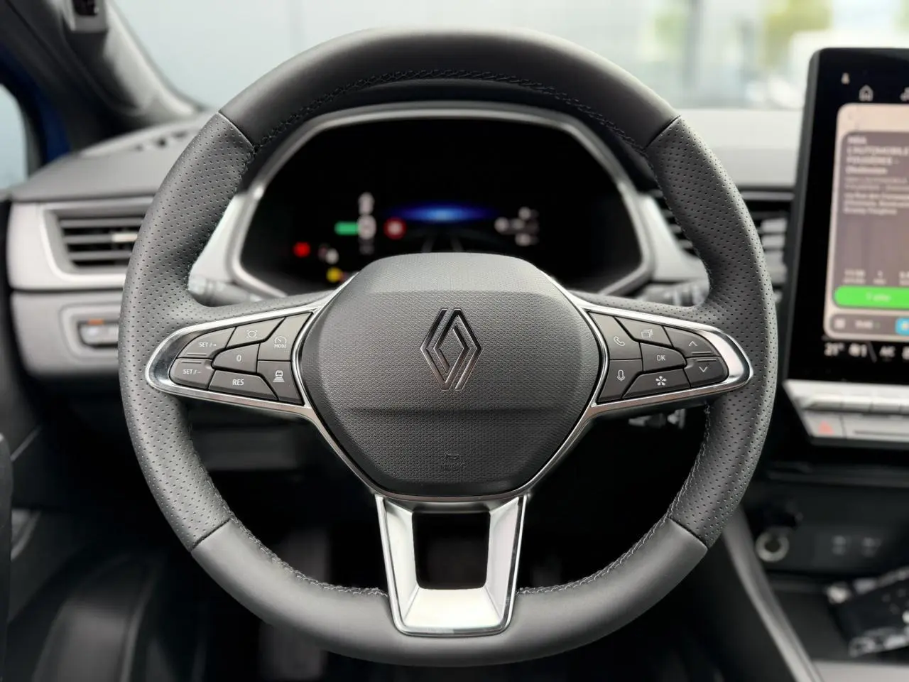 Volant en cuir perforé Renault Captur 2026 vu de face avec commandes intégrées et tableau de bord numérique flou.