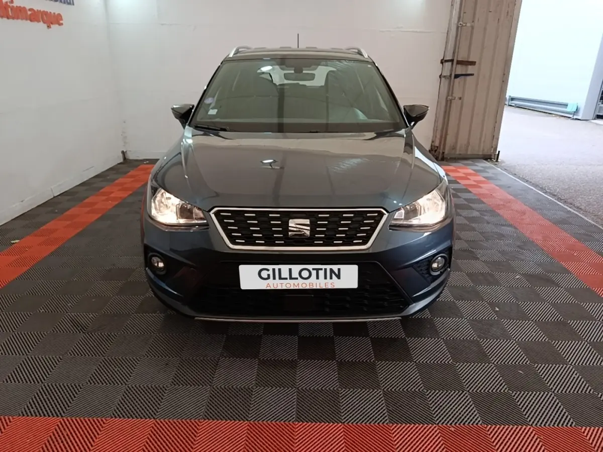 Vue avant d'un SEAT Arona gris clair avec calandre chromée et phares allumés dans un garage.