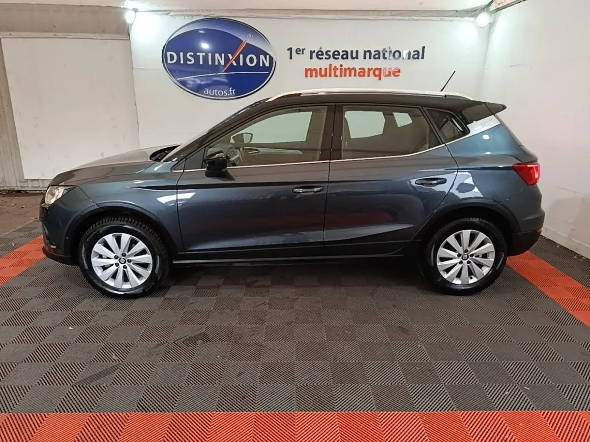Vue latérale droite d'un SEAT Arona gris foncé stationné en intérieur avec jantes argentées et toit noir.
