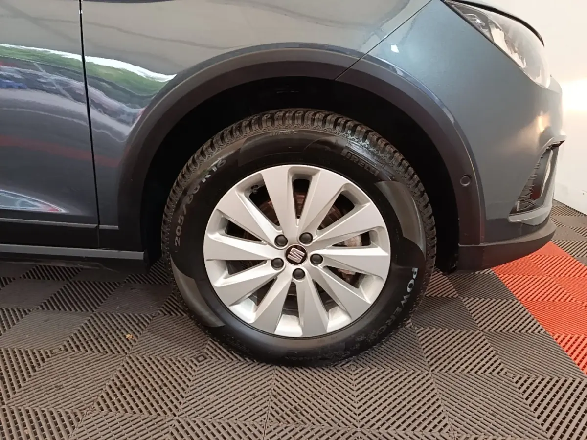 Gros plan sur la roue avant droite d’un SEAT Arona gris clair, avec jante alliage et logo central visible.