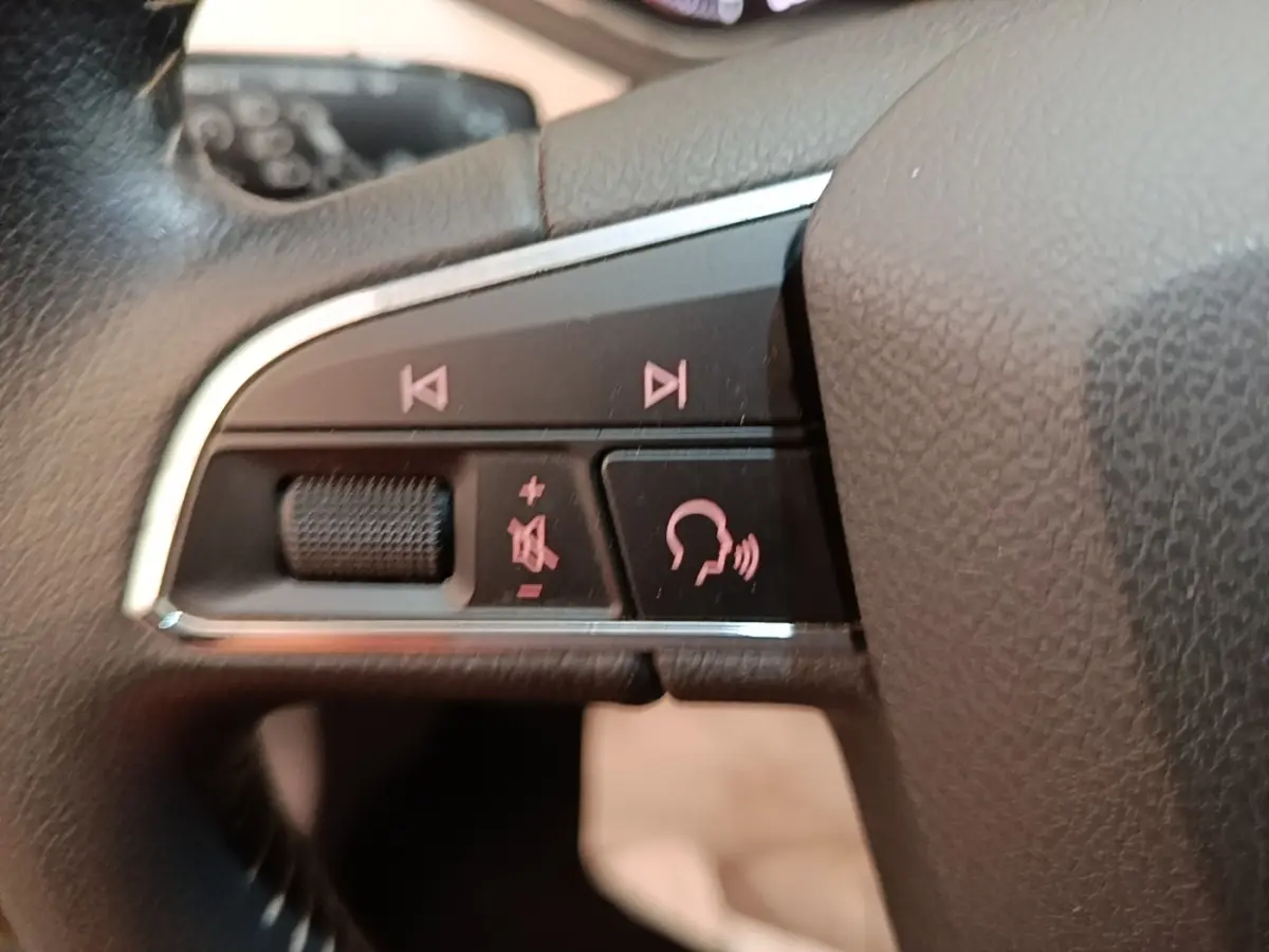 Gros plan sur les commandes vocales et audio sur le côté gauche du volant en cuir noir du SEAT Arona gris clair.
