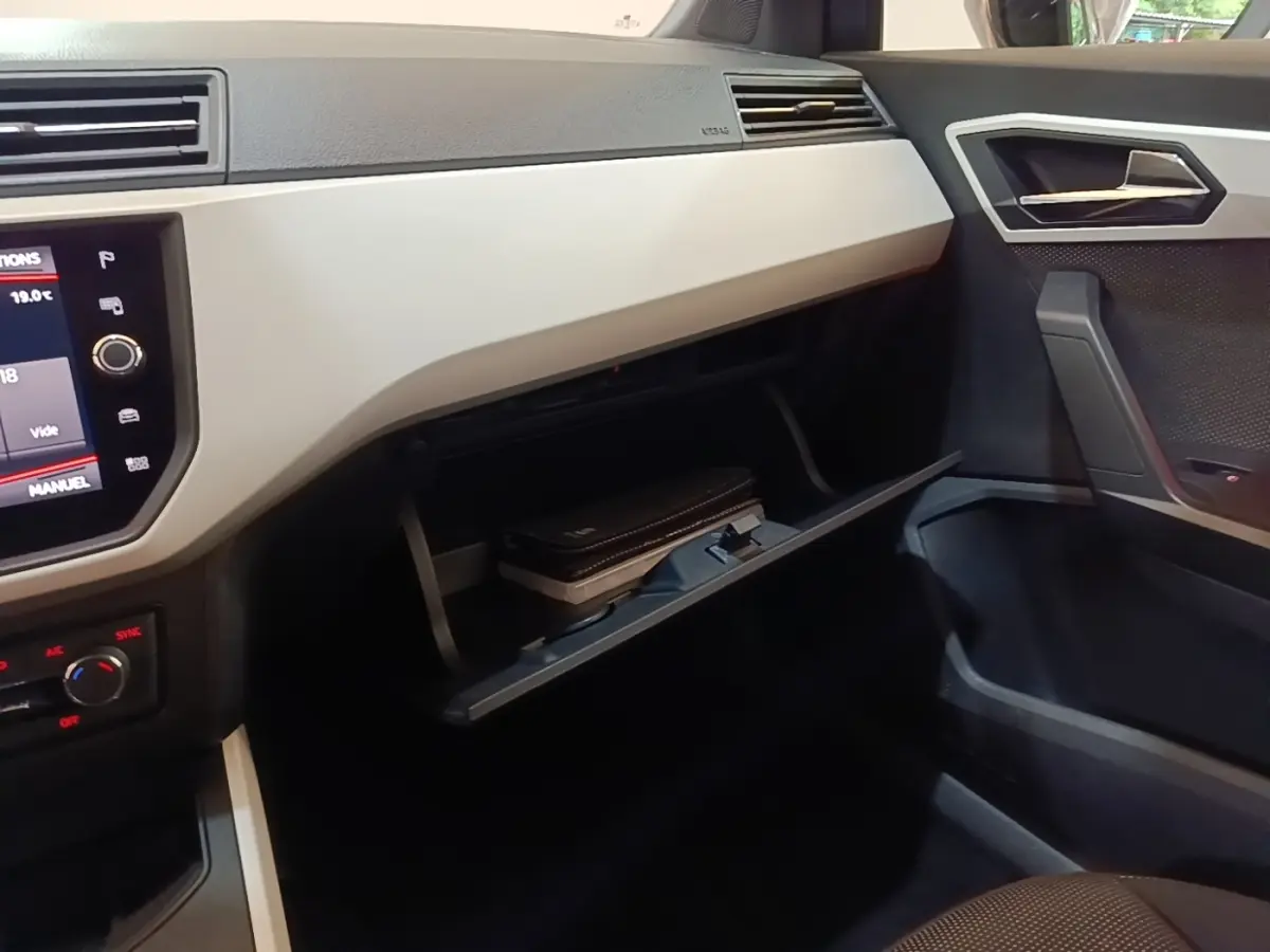 Intérieur côté passager du SEAT Arona 2019, tableau de bord clair avec boîte à gants ouverte et écran tactile visible.