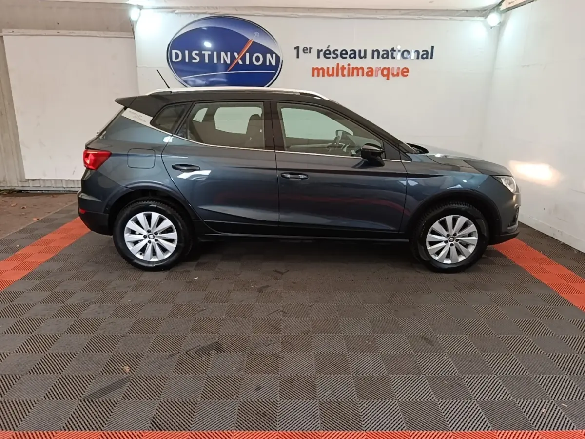 Vue latérale droite d'un SEAT Arona gris clair 2019 garé en intérieur avec jantes argentées et toit noir.
