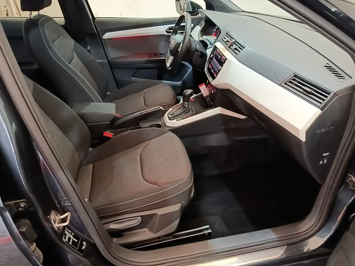 Vue intérieure côté conducteur du SEAT Arona 2019, sièges tissu gris foncé et tableau de bord clair avec écran tactile.