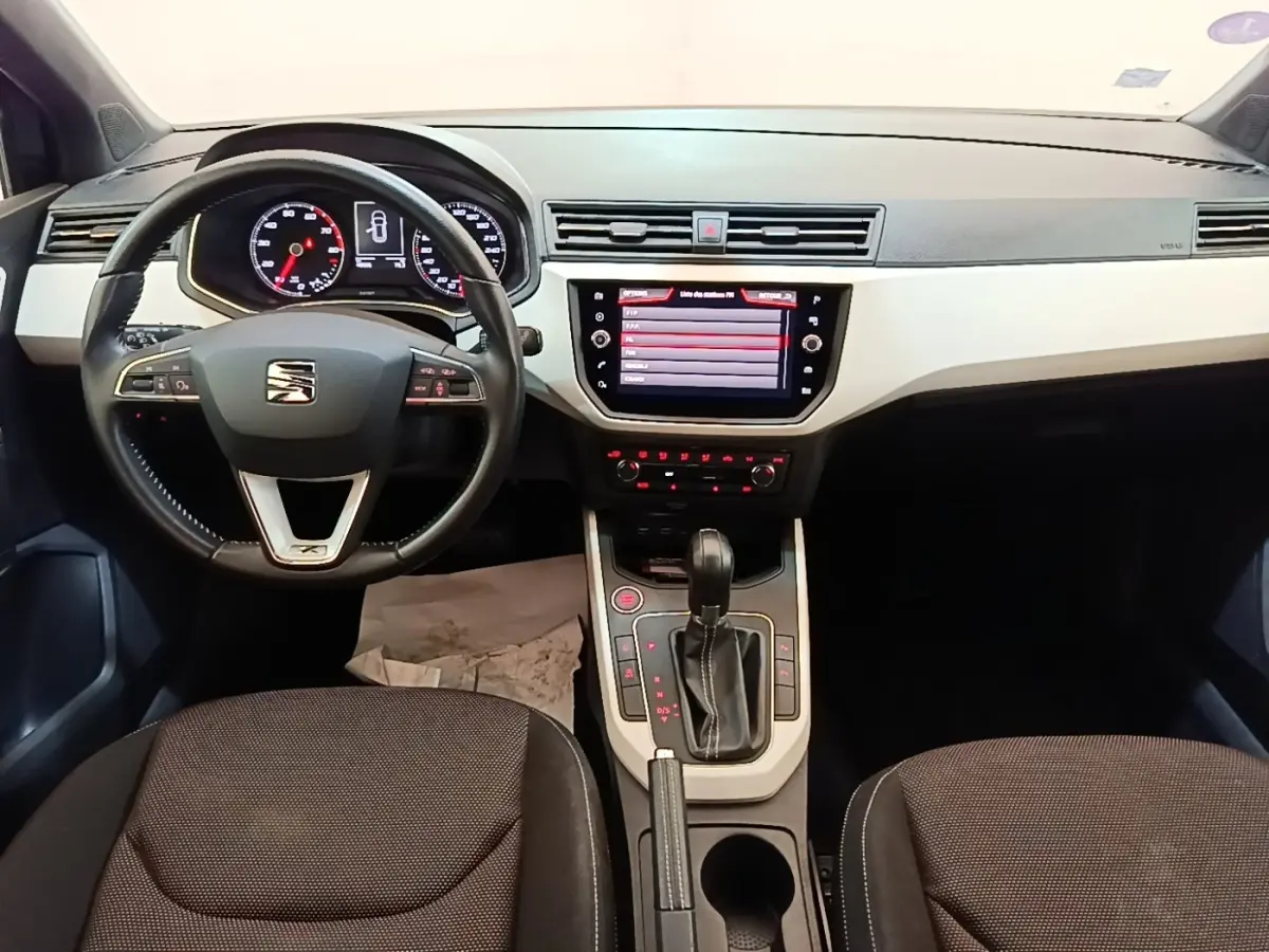 Vue intérieure frontale du tableau de bord et volant noir de la SEAT Arona 2019 avec écran tactile central allumé.