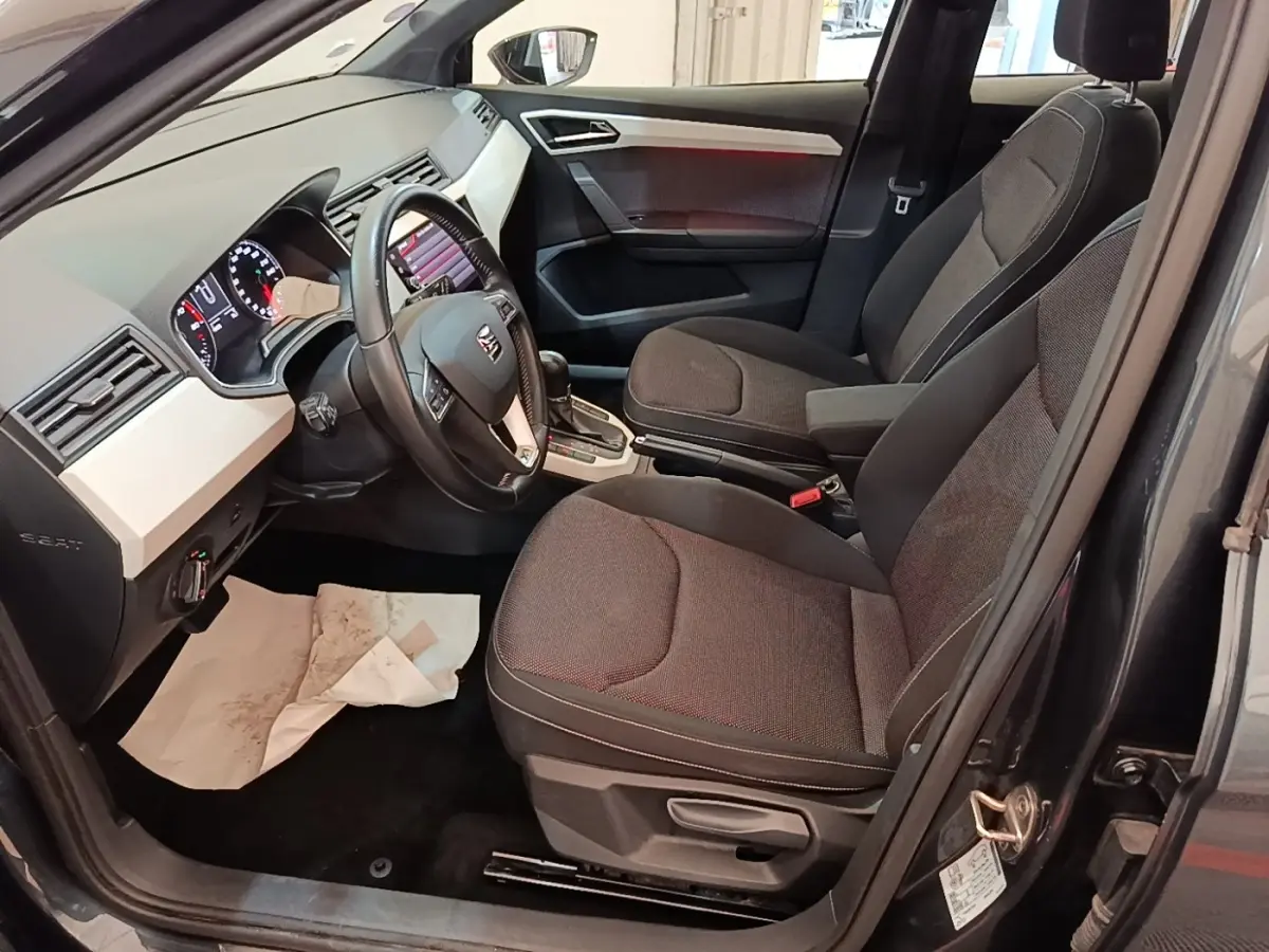Vue intérieure côté conducteur de la SEAT Arona gris clair 2019, avec tableau de bord et sièges tissu noirs.