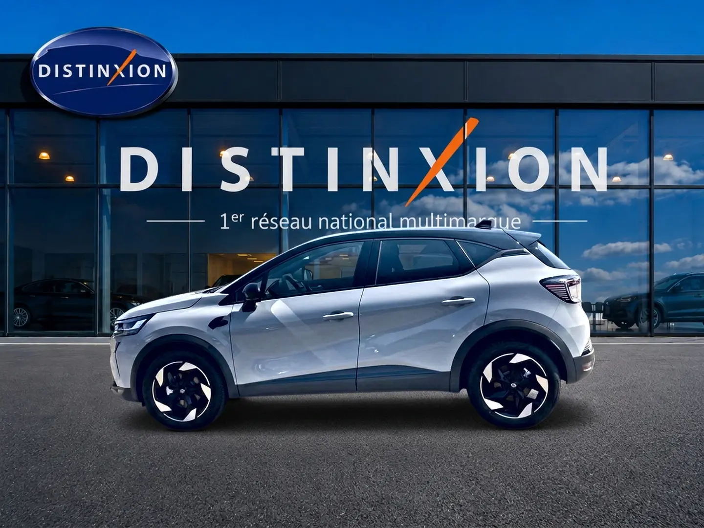 Profil latéral gauche du Renault Captur 1.2 TCe 115 Techno 2026 en couleur Rafale avec toit noir devant une vitrine Distinxion.