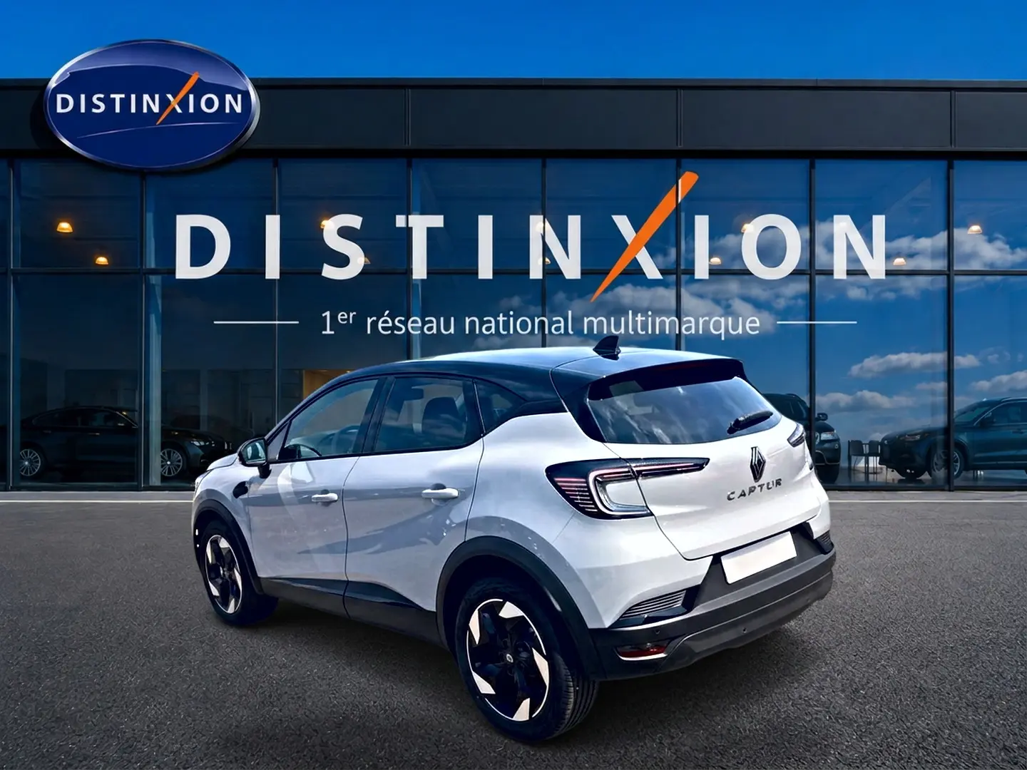 Vue 3/4 arrière droite du Renault Captur 2026 blanc Rafale avec toit noir et jantes alu noires devant un bâtiment vitré Distinxion.