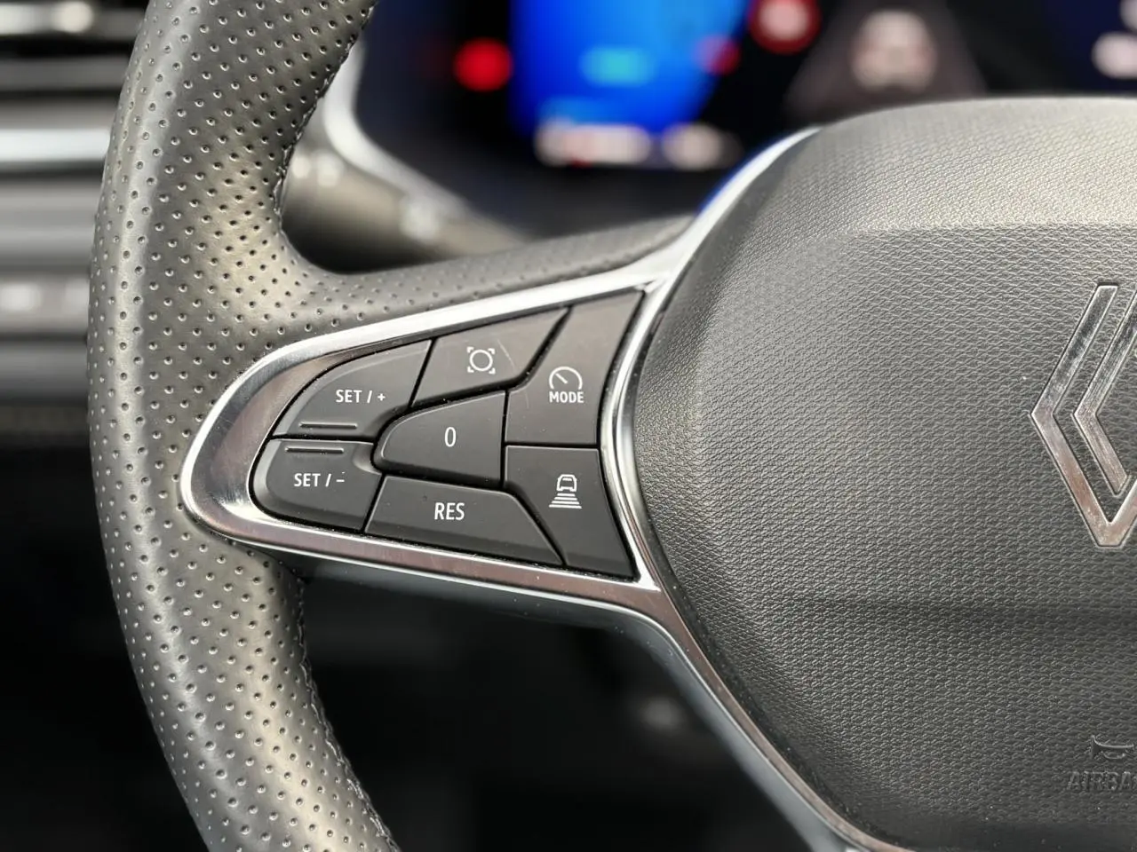 Gros plan sur la partie gauche du volant perforé du Renault Symbioz 2025, avec commandes de régulateur et logo Renault.