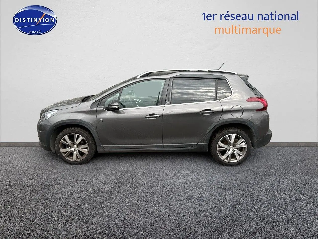 Peugeot 2008 gris platinium vue de profil côté gauche, avec jantes alliage et barres de toit visibles.