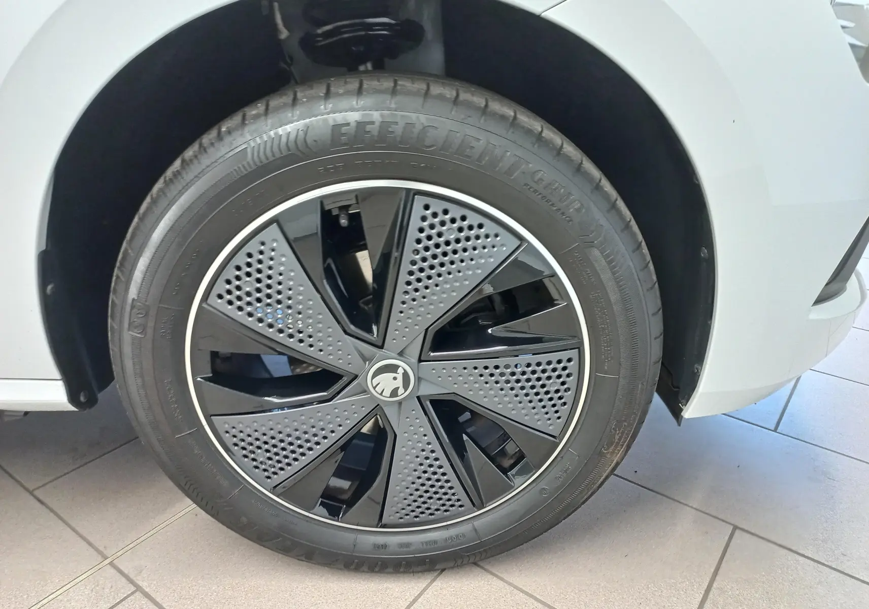 Gros plan sur la roue avant gauche du Skoda Kamiq 2025 blanc Lune avec jante noire au design perforé distinctif.