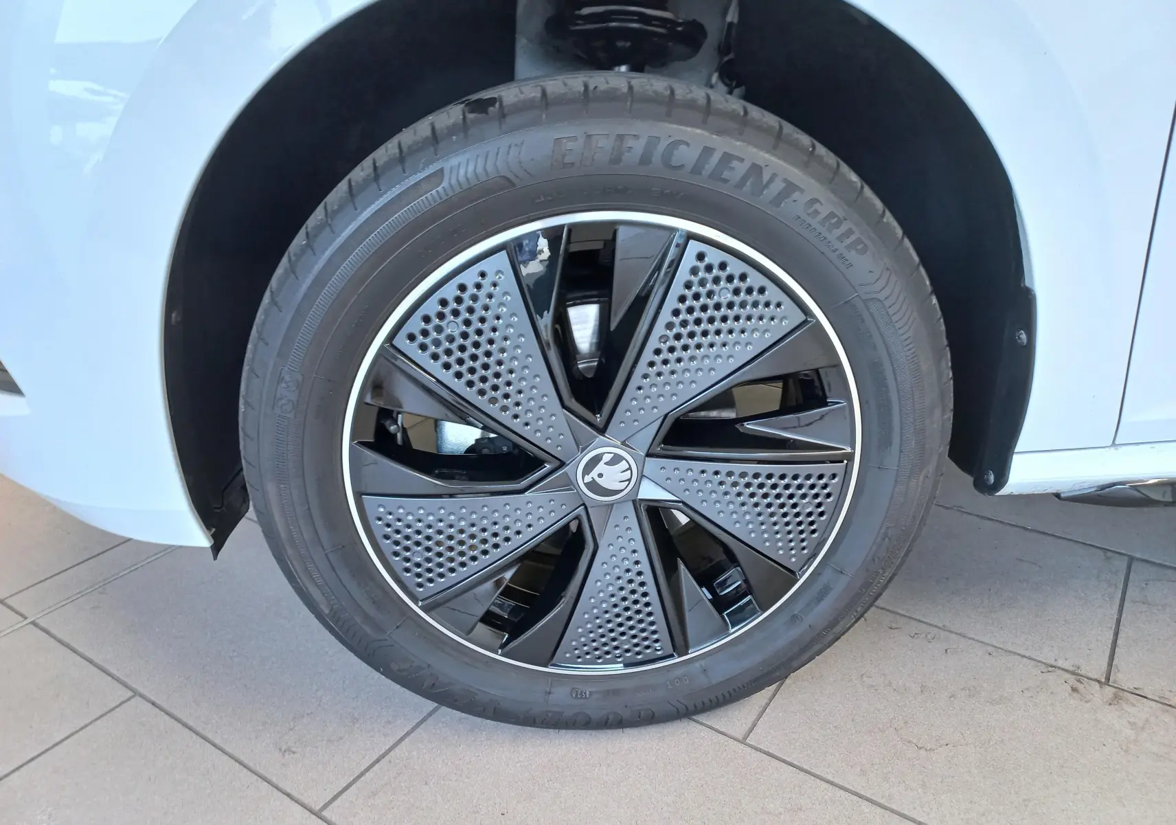 Gros plan sur la roue avant gauche du Skoda Kamiq blanc Lune avec jante noire et grise au design perforé.