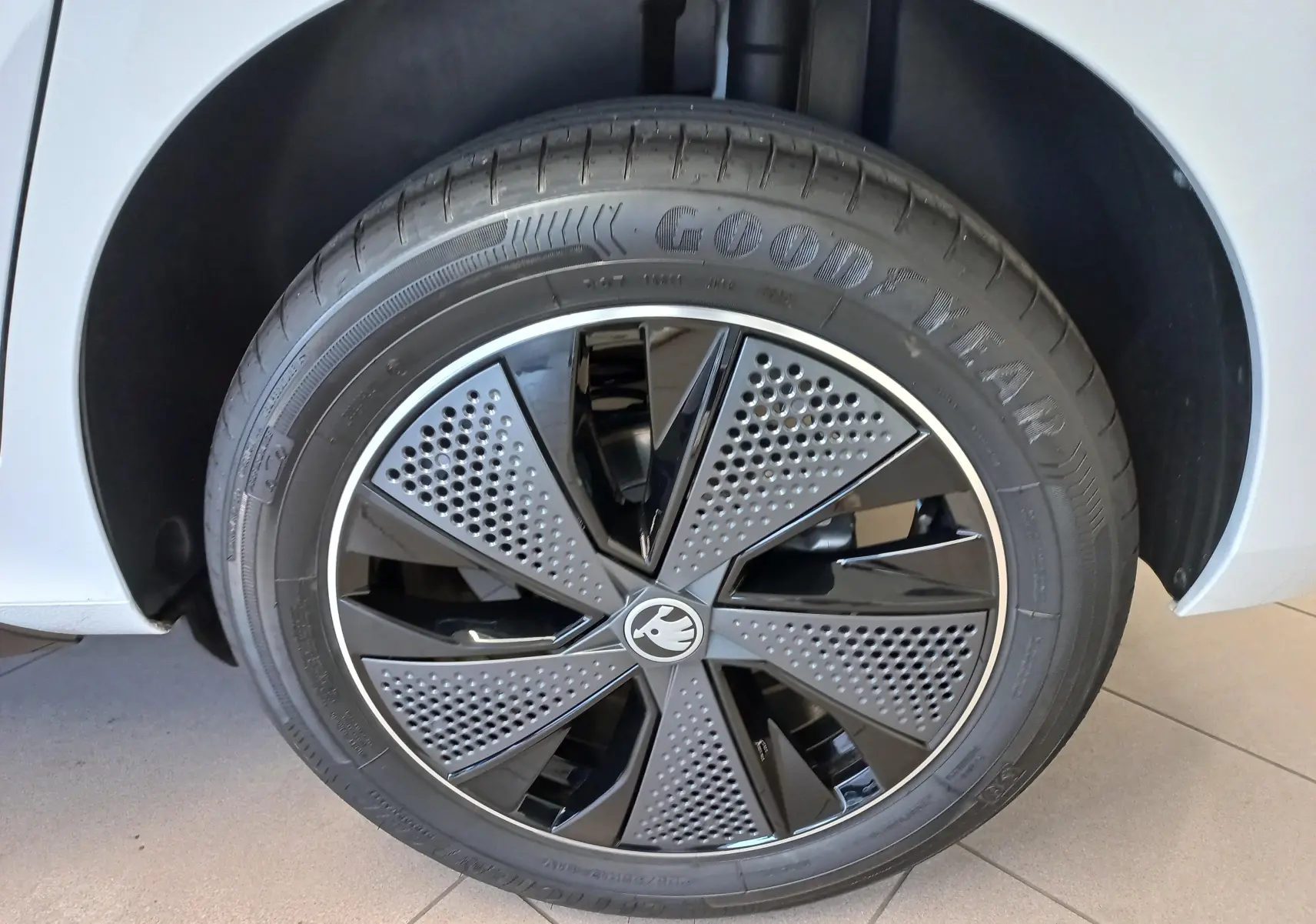 Gros plan sur la roue avant droite du Skoda Kamiq blanc Lune avec jante noire et grise au design perforé.