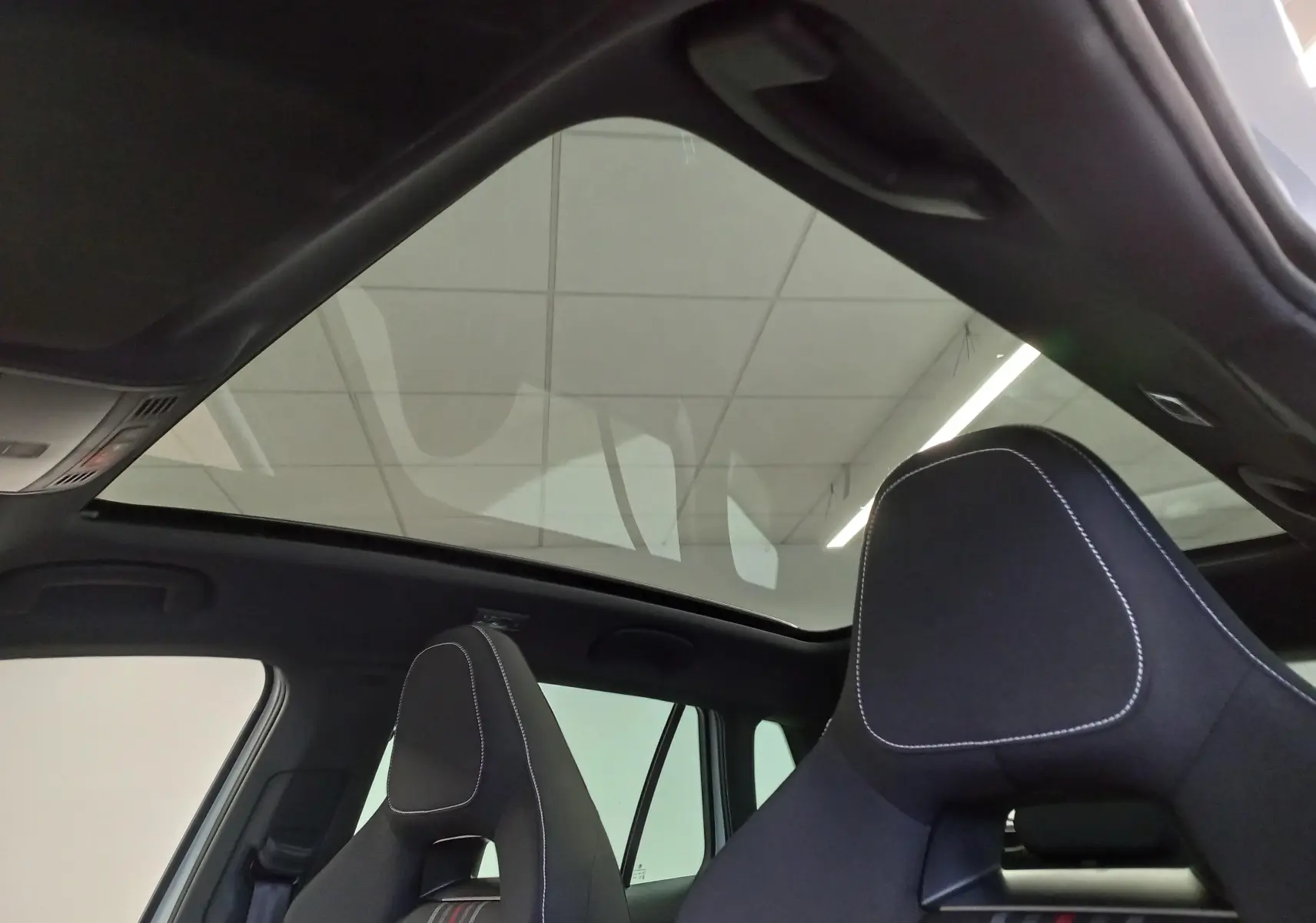 Toit panoramique en verre et sièges avant noirs avec surpiqûres blanches dans un Skoda Kamiq Blanc Lune 2025.