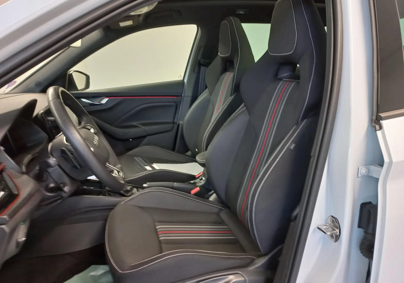 Intérieur côté conducteur du Skoda Kamiq blanc Lune 2025 avec sièges sport noirs à surpiqûres blanches et bandes rouges.
