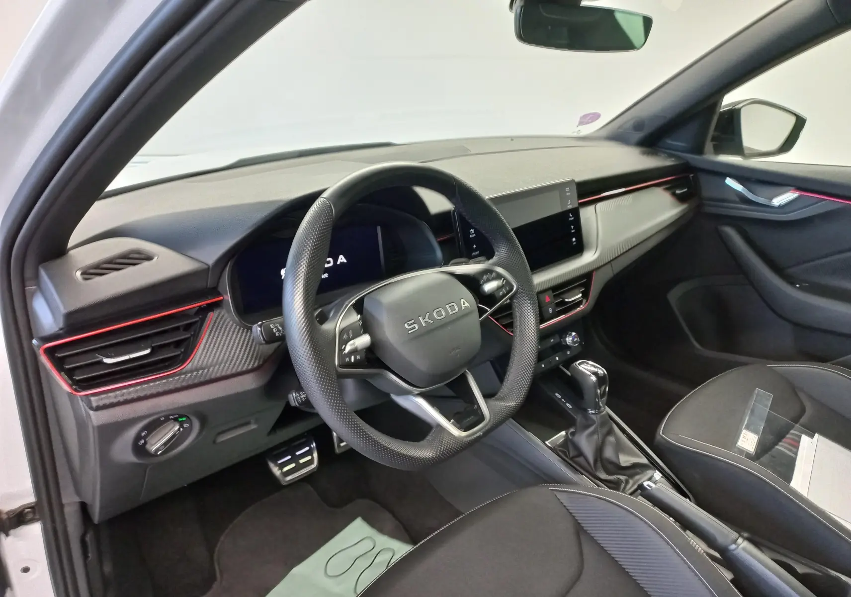Intérieur du Skoda Kamiq 2025 en vue côté conducteur, avec tableau de bord noir et éclairage d'ambiance rouge.