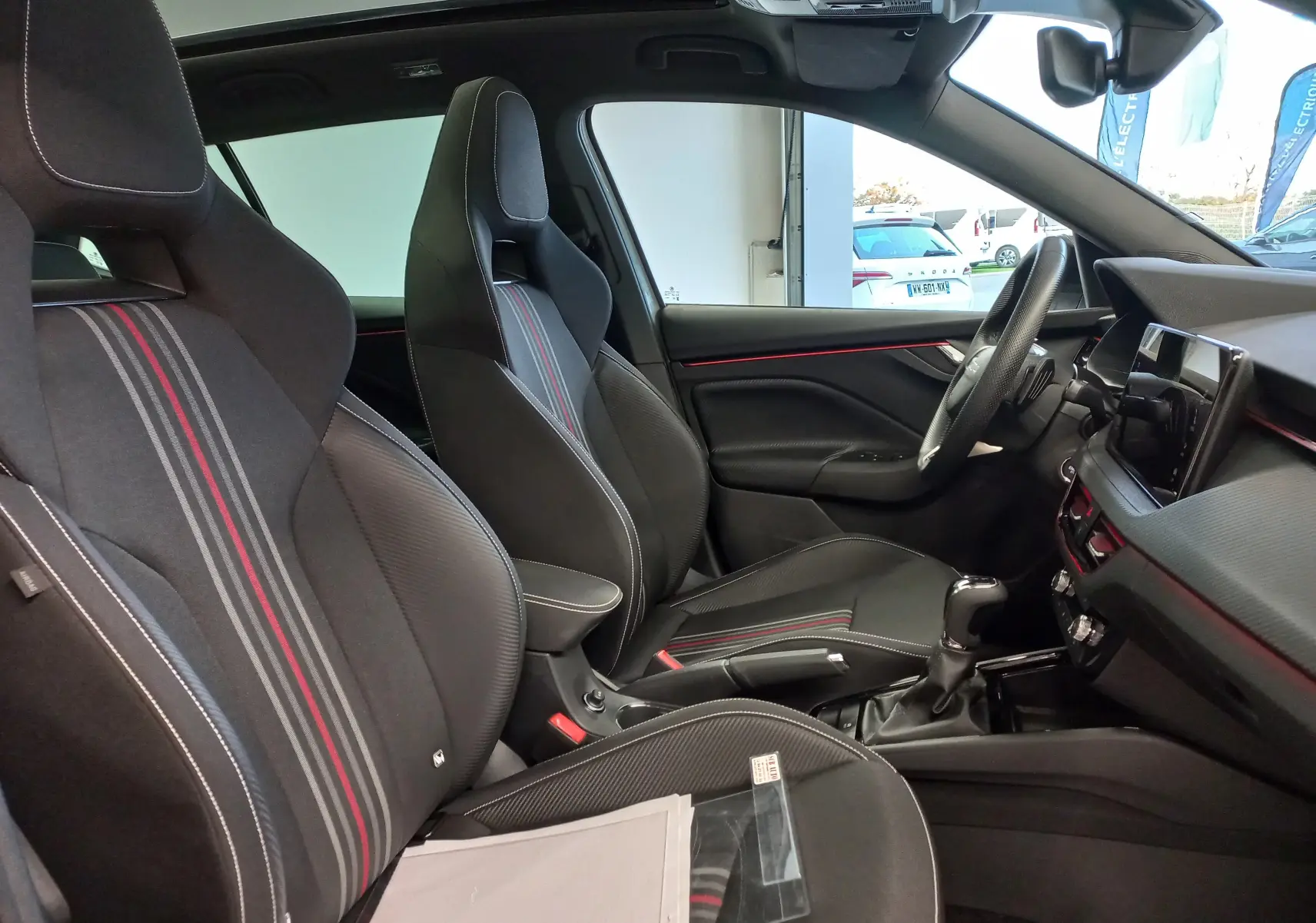 Intérieur du Skoda Kamiq 2025 en vue côté gauche, sièges sport noirs avec surpiqûres rouges et tableau de bord moderne.