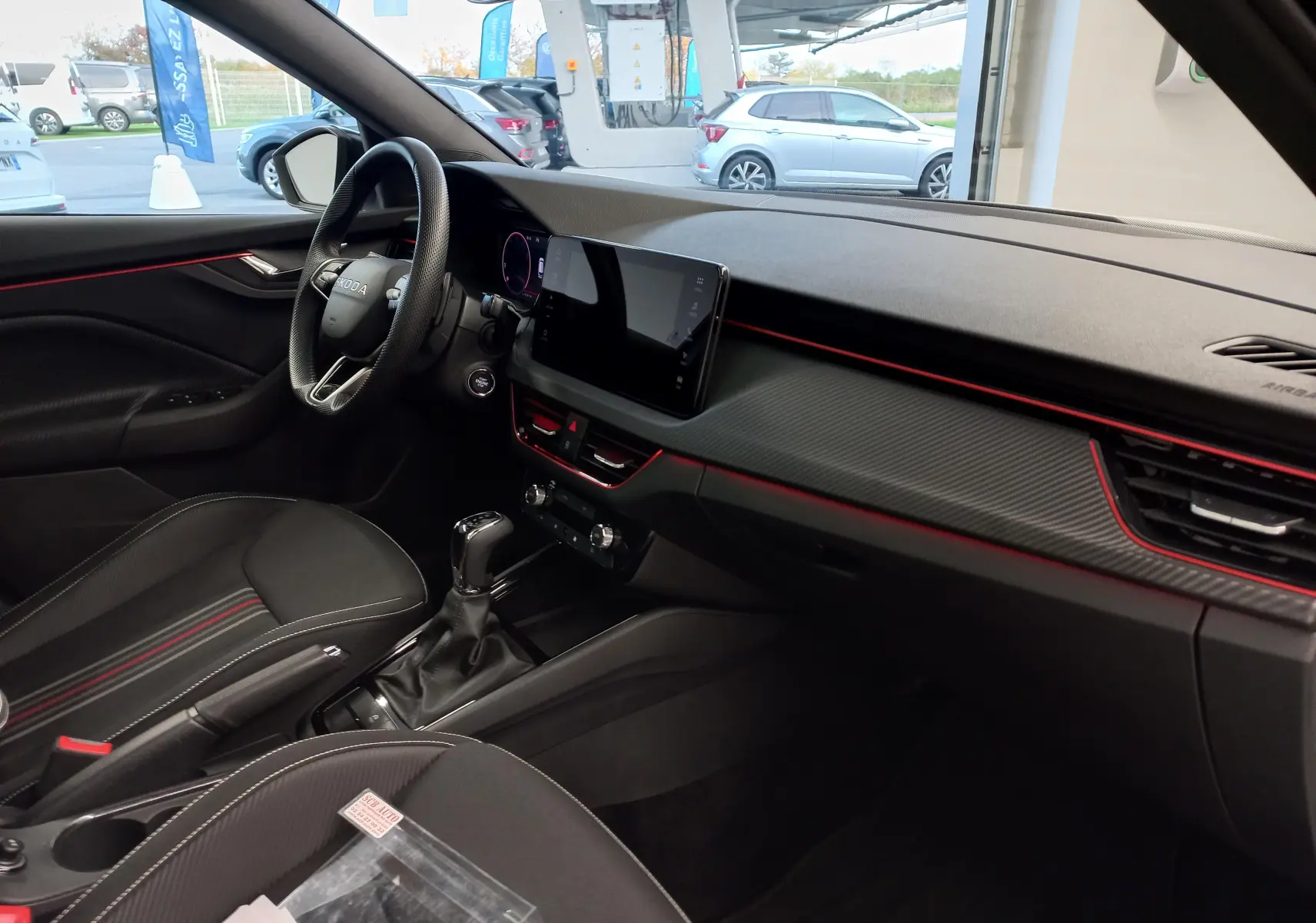 Intérieur côté conducteur du Skoda Kamiq 2025 blanc Lune, avec tableau de bord noir et touches rouges sportives.