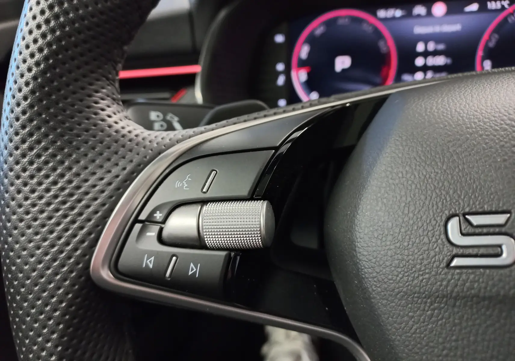 Gros plan sur les commandes gauche du volant perforé du Skoda Kamiq 2025 avec molette métallique et logo S visible.